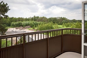 Utsikt från balkong mot skog och grönområde under molnig himmel