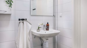 Litet badrum med handfat, spegel och vita kaklade väggar