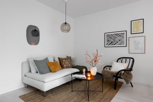 Vardagsrum med vit soffa, svart fåtölj och soffbord, dekorerat med kuddar, ljus och tavelvägg