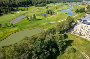 Flygvy över en golfbana med dammar, gröna fairways och ett flerfamiljshus intill