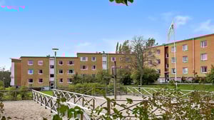 Flerfamiljshus i tegel med sandlåda och grön innergård under klarblå himmel