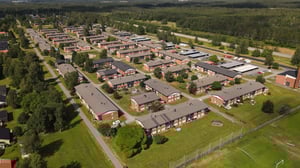 Flygvy över ett bostadsområde med flerfamiljshus, gröna innergårdar och omgivande skog