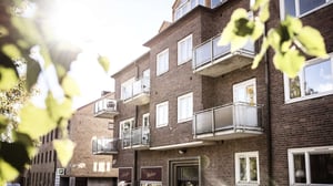 Flerbostadshus i tegel med balkonger och grönska i förgrunden