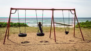Barn som gungar på en bildäcksgunga vid stranden, med havet i bakgrunden