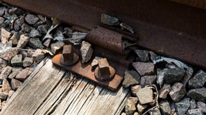 Närbild av rostig järnvägsräls med ballaststen och träslipers