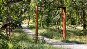 Gångstig genom grönskande skog med en rusten metallram vid sidan av stigen