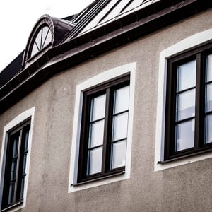 Fasad på en grå byggnad med vita fönsteromfattningar och svart tak