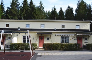 Radhuslänga med beige fasad, röda entrédörrar och träd framför