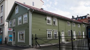 Grönt flerfamiljshus med vita fönster och svart staket framför