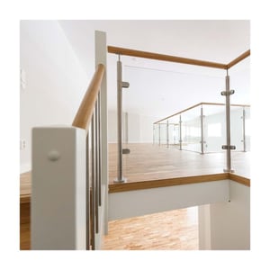 Ljust trapphus med glasräcke, vita väggar och trägolv