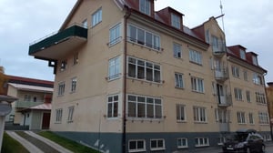 Flerfamiljshus med beige fasad, balkonger och parkerad bil utanför