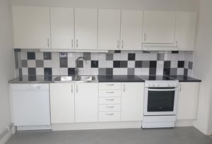 Inflyttningsklar lägenhet med vitt kök, svart bänkskiva, kaklat stänkskydd och vit spis