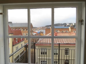 Utsikt över hustak och byggnader från ett fönster med balkongräcke i förgrunden