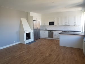 Inflyttningsklar lägenhet med öppen planlösning, vita köksluckor, rostfri kyl och frys samt träliknande golv