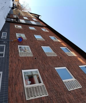 Flerbostadshus i rött tegel med vita fönsterluckor längs en snötäckt gata