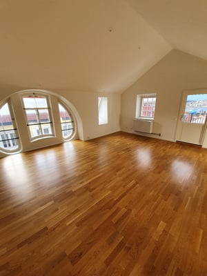 Inflyttningsklar lägenhet med tomt rum och trägolv, stora fönster och balkongdörr