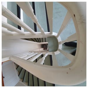 Vit spiraltrappa med vita räcken och grått golv