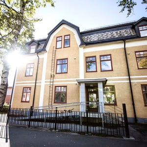 Flerbostadshus i ljusgul puts med mörkt tak, vita detaljer och entré med ramp