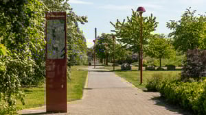 Promenadstig i grön parkmiljö i Helsingborg med skylt och röda gatlyktor längs gångvägen