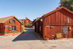 Röda trähus längs en smal gata i Strängnäs i ett soligt kvarter med svensk flagga och caféskyltar