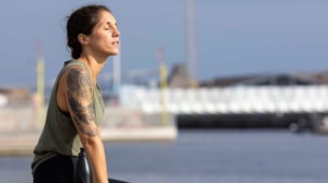 Profilbild av en kvinna med tatuering på armen vid vattnet