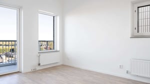 Inflyttningsklart rum med vita väggar, ljusa trägolv och stora fönster med balkongutgång