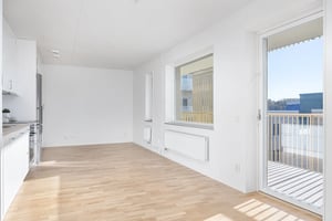 Inflyttningsklar lägenhet med ljus öppen planlösning, vita väggar och träfärgat golv. Balkongdörr och fönster släpper in mycket dagsljus