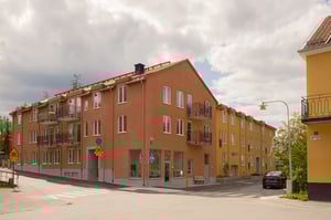 Flerfamiljshus i orange och gula fasader med balkonger vid en gatukorsning