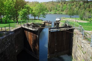 Sluss med båt i bakgrunden vid en sjö, omgiven av grönskande träd och natur