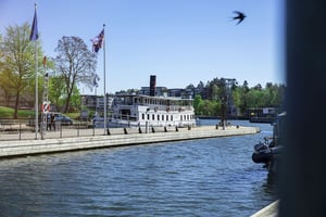 Båtbrygga vid vatten med en vit ångbåt och flaggor i solsken