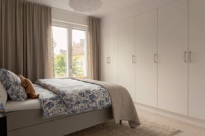 Inflyttningsklart sovrum med stor garderobsvägg, dubbelsäng och fönster med gardiner