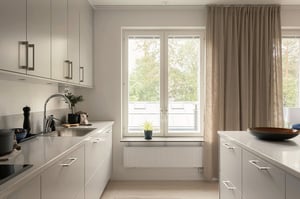 Ljust vitt kök med arbetsyta, diskho, köksö och fönster med beige gardiner. Inflyttningsklart