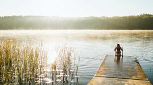 Kvinna badar från en brygga i en stilla sjö i morgondimma