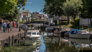 Båtkanal med förtöjda småbåtar, promenadstråk och historiska hus omgivna av grönska