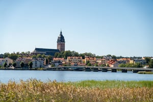 Utsikt över Strängnäs vid vatten med kyrktorn, bro och färgglada hus i solsken
