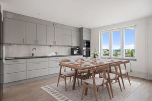 Inflyttningsklart kök och matplats med gråa skåpsluckor, träbord och stora fönster