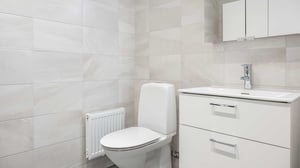 Inflyttningsklart badrum med vita kaklade väggar, toalett, handfat och badrumsskåp