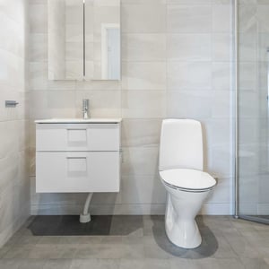 Badrum med vit kommod, toalett och duschhörna i kaklat utrymme