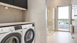 Tomt rum med tvättmaskin och torktumlare, ljusa kaklade väggar och utgång till balkong