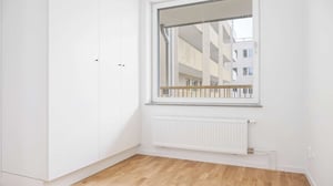 Inflyttningsklar lägenhet med ljusa väggar, trägolv, garderober och stort fönster mot innergård
