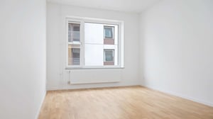 Inflyttningsklart rum med ljusa väggar, trägolv och ett stort fönster