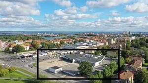 Flygvy över en stad med bostadsområden, vatten och en större byggnad i förgrunden