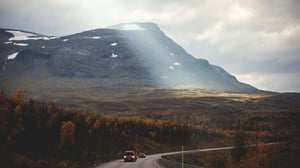 Bergslandskap med väg, skog och solstrålar över en fjälltopp