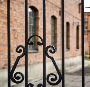 Svart smidesgrind framför en tegelbyggnad med fönster i Västerås