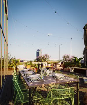 Uppdukat matbord på en takterrass med gröna stolar, växter och utsikt över stadssilhuetten