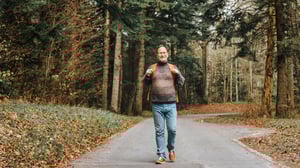 En man med ryggsäck promenerar på en skogsväg