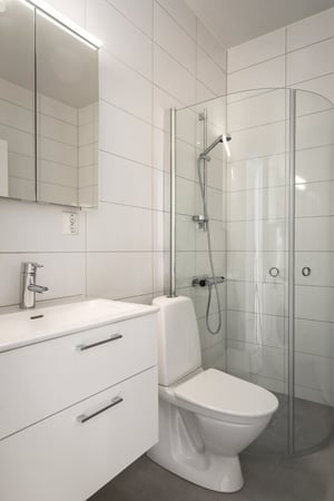 Inflyttningsklart badrum med vit kommod, toalett och duschhörna med glasväggar