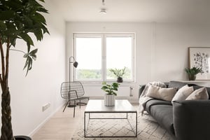 Vardagsrum i en inflyttningsklar lägenhet med soffa, soffbord, växter och stor fönsteröppning