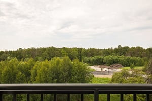 Utsikt från balkong över grön skog och en byggarbetsplats i fjärran