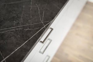 Närbild av svart marmorskiva med vita ådror och vit kökslucka med handtag